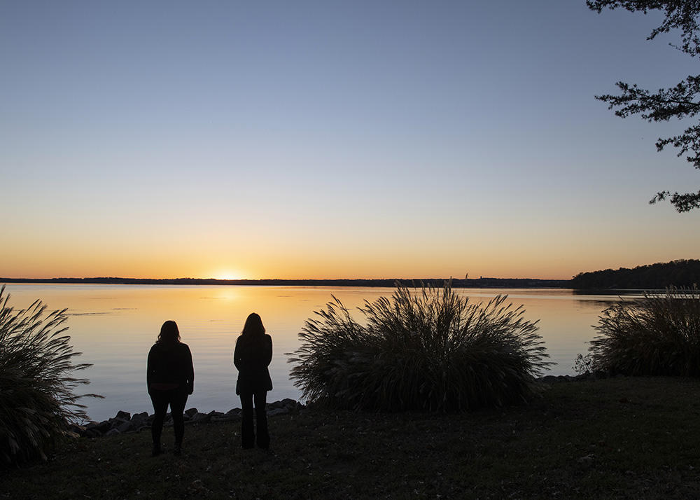 Two students standing in silhouette in front of the lake at Point of View International Retreat
